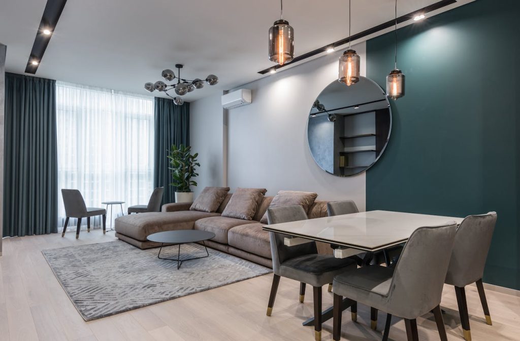 pexels-photo-6585598 Interior of modern living room with comfortable big sofa and dining zone decorated with creative lamps and mirror in daylight
